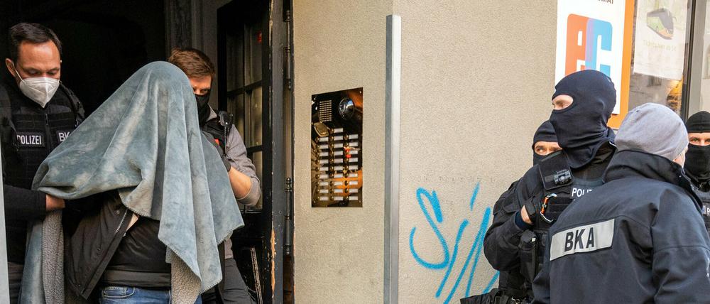 Ein Mann wird bei einer Razzia in Berlin, mit einer Decke über dem Kopf, von der Polizei abgeführt.