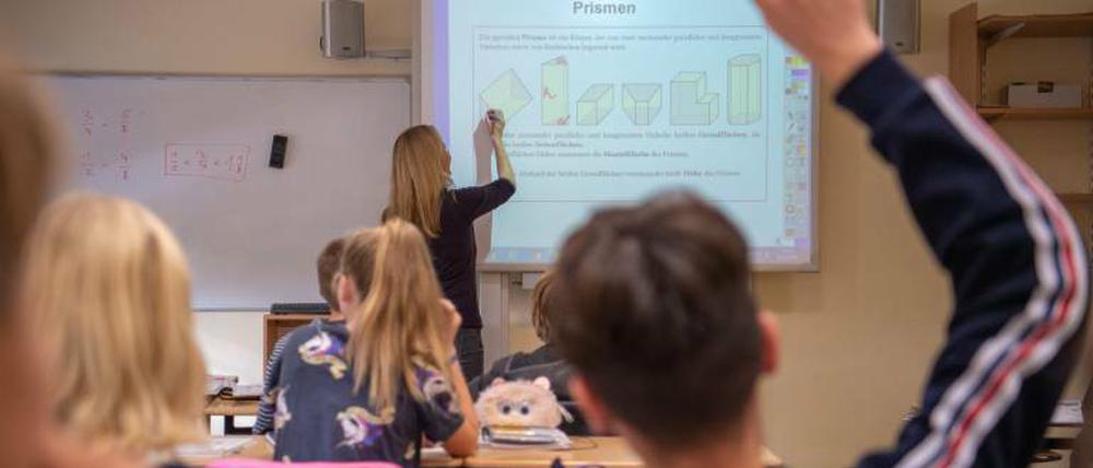 Schüler sitzen in einer Klasse, in der die Lehrerin vorne am Smartboard steht.