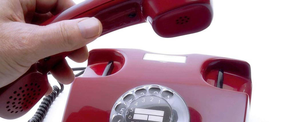 Hand, die an einem alten Wählscheiben-Telefon den Hörer abnimmt.