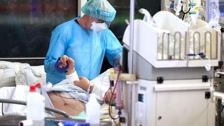 Ein Facharzt versorgt einen Covid-19-Patienten auf der Intensivstation der Leipziger Uniklinik und hält dessen Hand.
