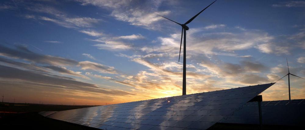 Windräder stehen hinter den Solarzellen einer Solarkraftanlage in Bayern. 