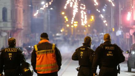 Böllerverbot: Polizisten und ein Rettungssanitäter stehen an einer Kreuzung und schauen auf ein Feuerwerk. (Archivbild)