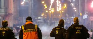 Böllerverbot: Polizisten und ein Rettungssanitäter stehen an einer Kreuzung und schauen auf ein Feuerwerk. (Archivbild)