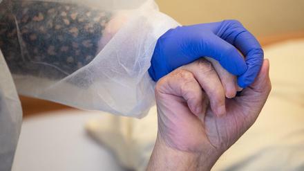 Eine Altenpflegerin in Schutzkleidung hält die Hand eines Bewohners. 