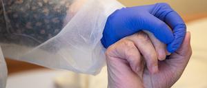 Eine Altenpflegerin in Schutzkleidung hält die Hand eines Bewohners. 