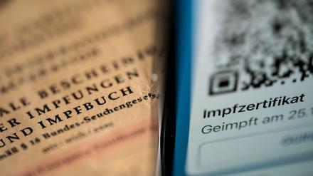 Ein Smartphone, auf dem ein Impfzertifikat in der Corona Warn App angezeigt wird, liegt auf einem Impfbuch (Symbolbild).