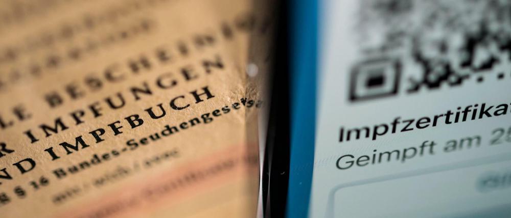 Ein Smartphone, auf dem ein Impfzertifikat in der Corona Warn App angezeigt wird, liegt auf einem Impfbuch (Symbolbild).