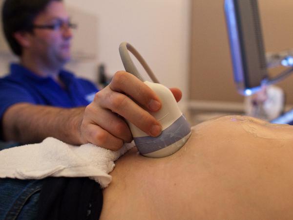 Ein Facharzt für Gynäkologie und Geburtshilfe untersucht in seiner Praxis für pränatale Diagnostik und Ultraschall in Berlin eine im dritten Monat schwangere Frau.