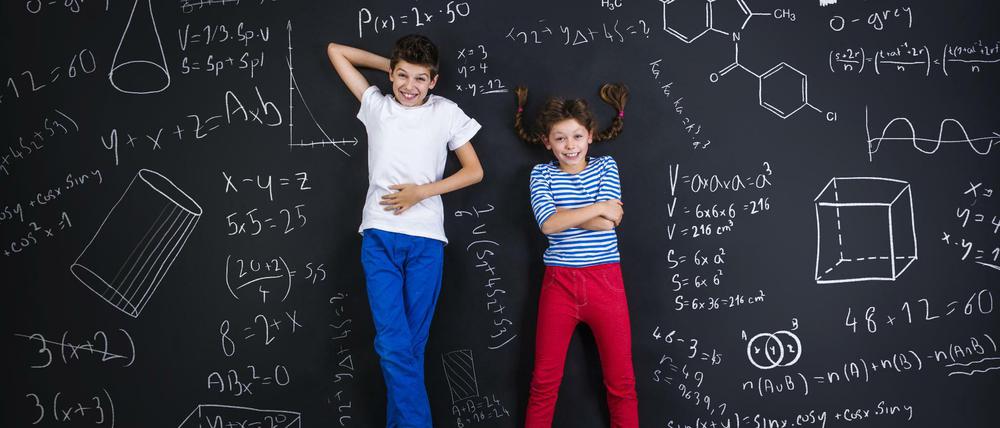 Ein Junge und ein Mädchen liegen lachend auf einer schwarzen Tafel, die mit mathematischen Formeln und Formen vollgeschrieben ist.
