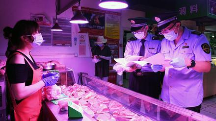 Mitarbeiter der Marktregulierungsverwaltung überprüfen an einem Marktstand in Peking die Lieferkette für Fleisch und die Einhaltung von Desinfektions-Maßnahmen, die aufgrund der Corona-Pandemie getroffen werden müssen.