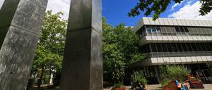 Zwei schwingende Metallsäulen vor einem Unigebäude.
