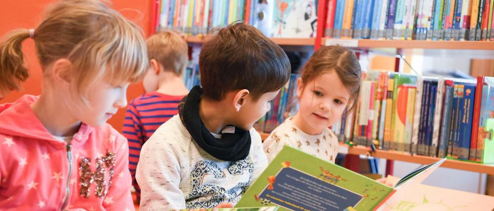 Zwei Schülerinen und ein Schüler lesen in der Schulbibliothek einer Schule Bücher.