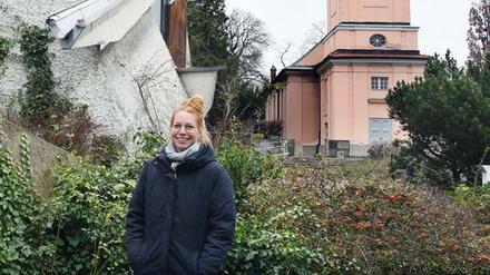 Pfarrerin Rebecca Cyranek steht am Gelände der Berliner Kirchengemeinde Alt-Schöneberg mit der alten und der modernen Kirche.