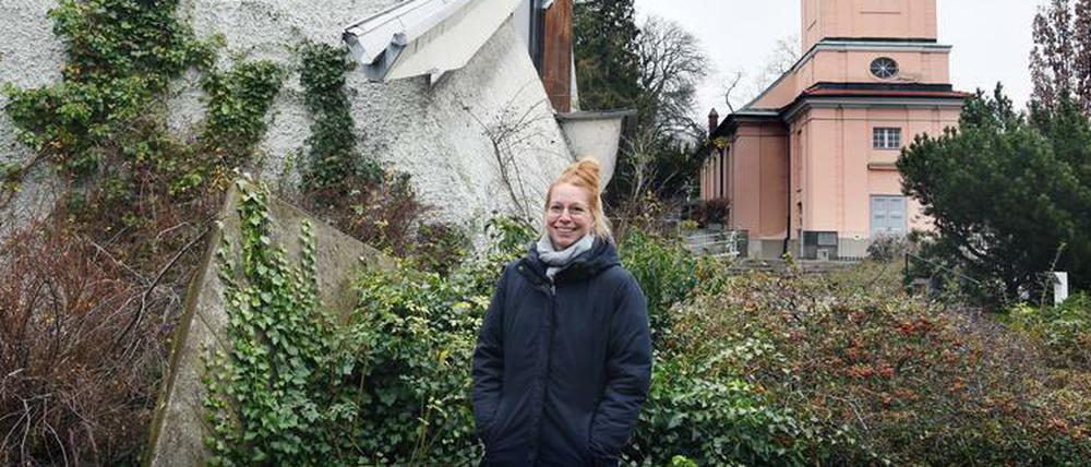 Pfarrerin Rebecca Cyranek steht am Gelände der Berliner Kirchengemeinde Alt-Schöneberg mit der alten und der modernen Kirche.