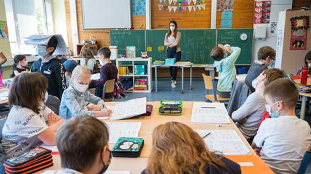 Eine Grundschullehrerin steht vor einer Grundschulklasse, alle Fragen einen Mund-Nasen-Schutz.