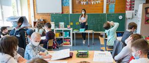 Eine Grundschullehrerin steht vor einer Grundschulklasse, alle Fragen einen Mund-Nasen-Schutz.