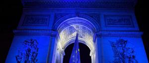 Menschen versammeln sich vor dem blau beleuchteten Arc de Triomphe in Paris, in dessen Bogen eine EU-Flagge hängt