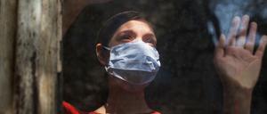 Eine Frau mit Maske schaut aus einem Fenster nach draußen.