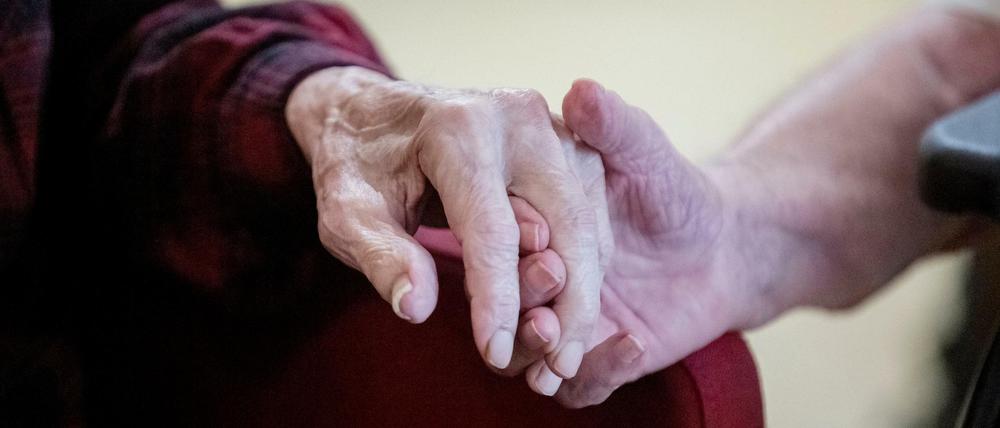 Eine Bewohnerin und ein Bewohner halten in einer betreuten Demenz-Wohngemeinschaft in Berlin Hände.