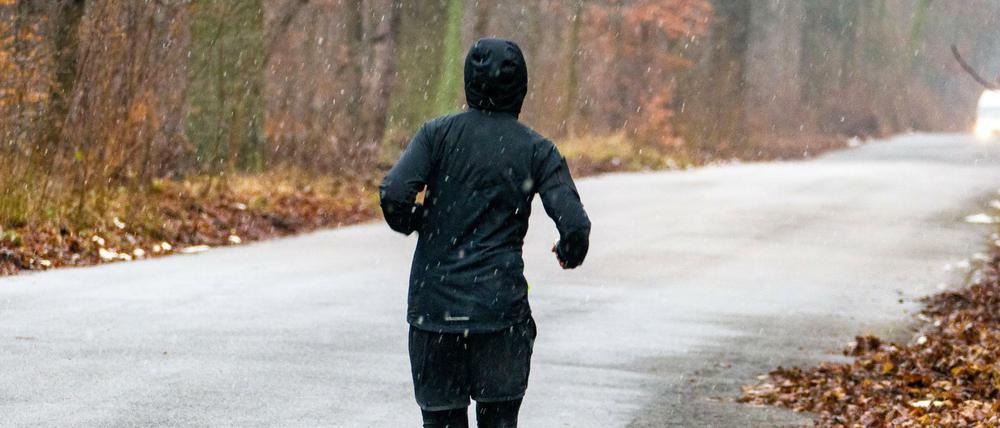 Ein junger Läufer auf einer leicht verschneiten Straße in einem Waldgebiet.