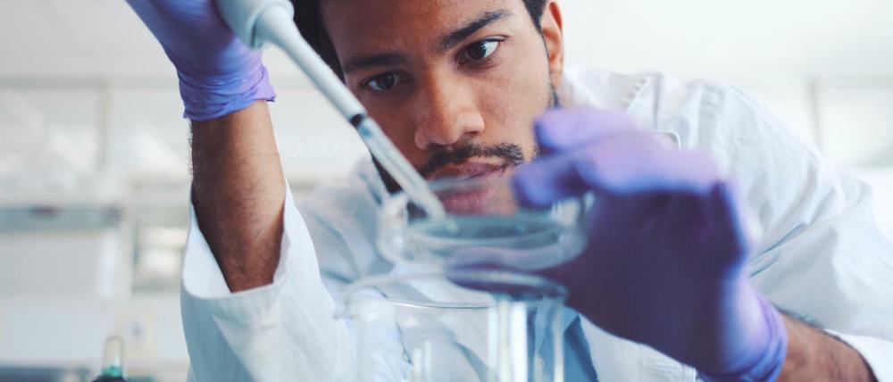 Ein junger Wissenschaftler hantiert im Labor mit Pipette und Petrischale.