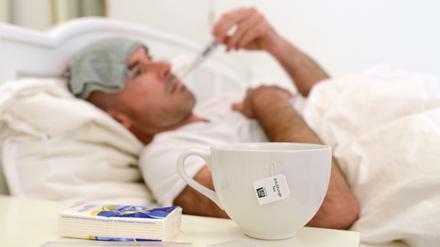 Ein Mann liegt im Bett und misst Fieber (Symbolbild).