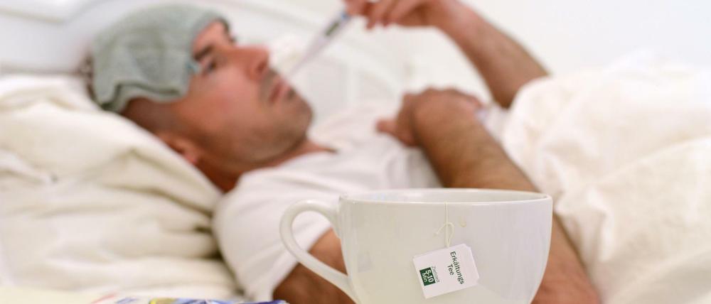 Ein Mann liegt im Bett und misst Fieber (Symbolbild).