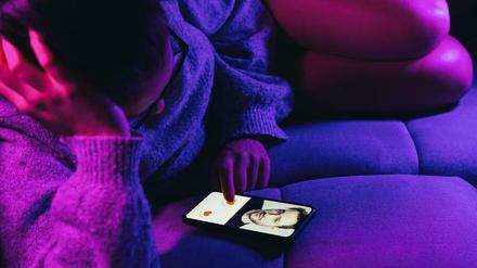 Eine Frau liegt auf dem Sofa und hat auf ihrem Smartphone eine Online Dating App offen.