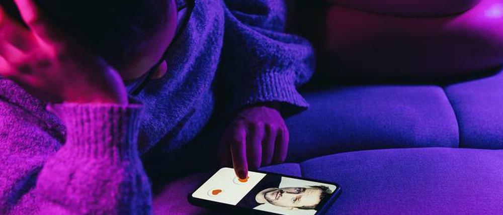 Eine Frau liegt auf dem Sofa und hat auf ihrem Smartphone eine Online Dating App offen.