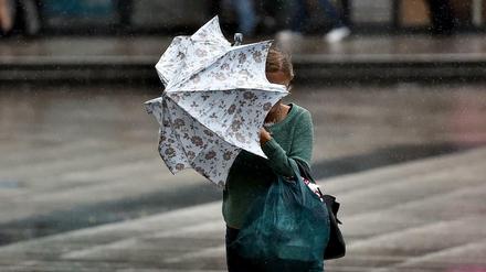 Eine junge Frauen kämpft in Berlin bei Starkwind mit einem Regenschirm.