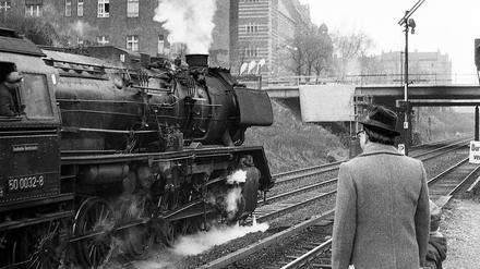 Eine Baureihe 50 fährt 1975 auf dem Ring. Vom S-Bahnsteig Prenzlauer Allee schauen Vater und Kind zu.
