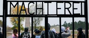 Hinter dem Lagertor mit dem "Schriftzug Arbeit macht frei" steht eine Gruppe von Jugendlichen auf dem Gelände des ehemaligen Konzentrationslagers.