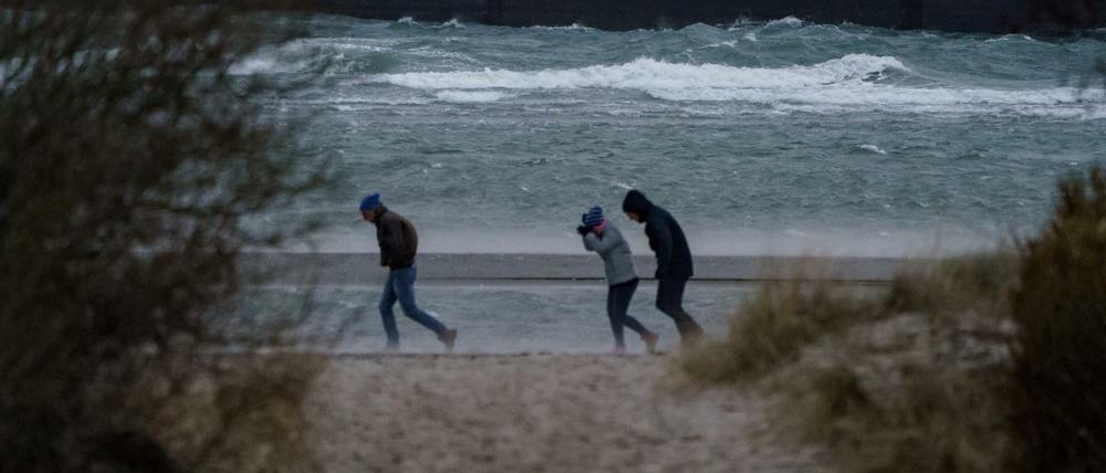 Spaziergänger stemmen sich gegen Windböen vor dem vom Wind aufgepeitschten Wasser am Ostsee-Strand.