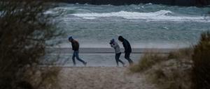 Spaziergänger stemmen sich gegen Windböen vor dem vom Wind aufgepeitschten Wasser am Ostsee-Strand.