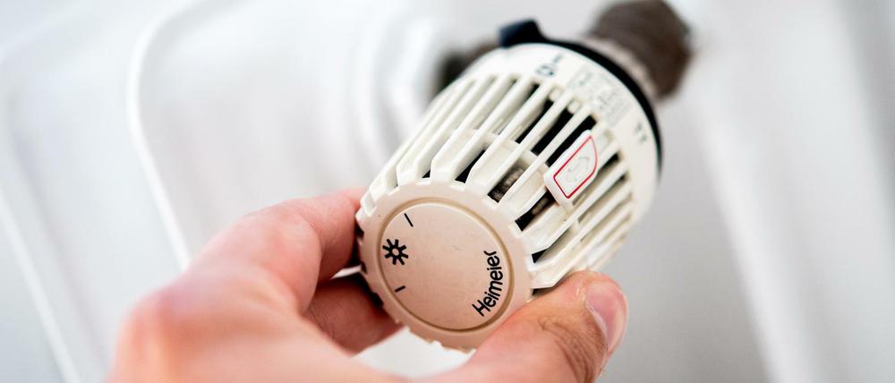 Ein Mann dreht in einer Wohnung am Thermostat einer Heizung.