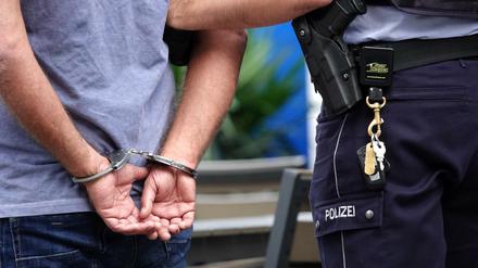 Ein Mann steht in Handschellen neben einem Polizisten. (Symbolbild)