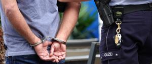 Ein Mann steht in Handschellen neben einem Polizisten. (Symbolbild)
