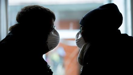 Ein Paar sitzt sich gegenüber. Freunde oder Familienmitglieder des Paares sind in Verschwörungsmythen verfangen und leugnen Corona.