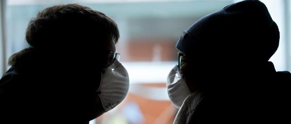 Ein Paar sitzt sich gegenüber. Freunde oder Familienmitglieder des Paares sind in Verschwörungsmythen verfangen und leugnen Corona.