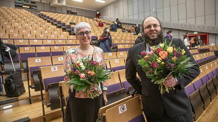 Eine Frau und ein Mann stehen mit Blumensträußen in der Hand in einem Hörsaal.