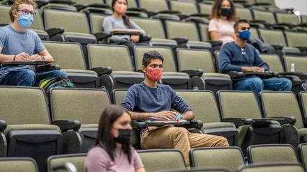 Studierende mit Mund-Nasen-Schutz sitzen mit großen Abständen voneinander in einem Hörsaal.