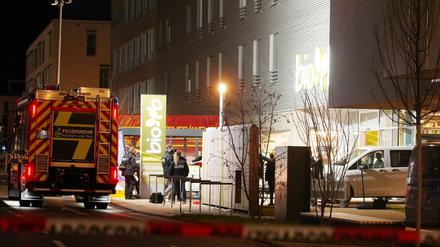 Polizisten und Feuerwehrleute stehen an einem Supermarkt. Dort sind zwei Menschen durch Schüsse ums Leben gekommen.