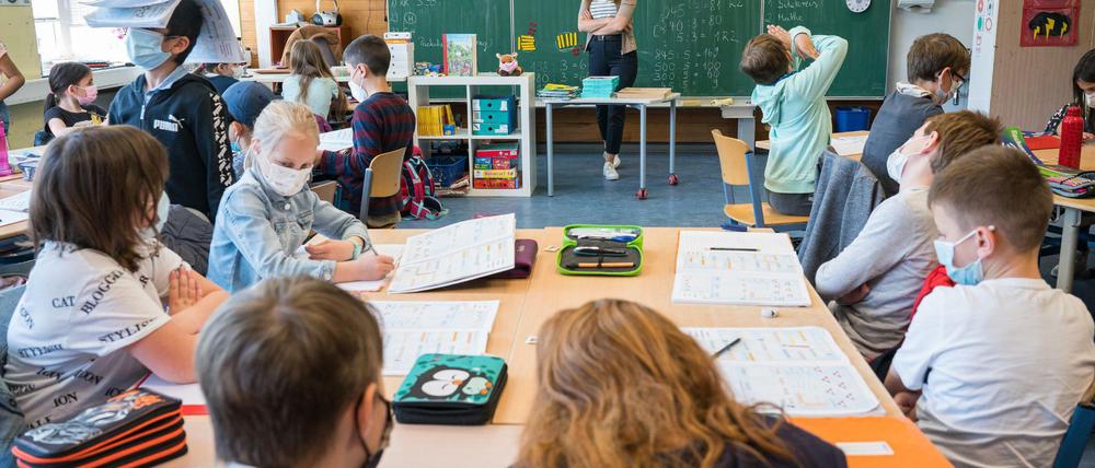 Kinder sitzen in einer Grundschule über ihren Aufgaben und tragen dabei Mund-Nasen-Schutz,