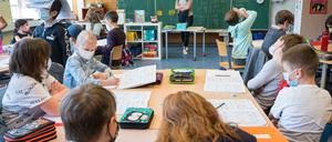 Kinder sitzen in einer Grundschule über ihren Aufgaben und tragen dabei Mund-Nasen-Schutz,