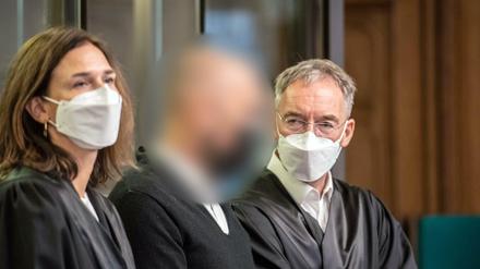 Der Angeklagte steht im Gerichtssaal zwischen seinen Anwälten.