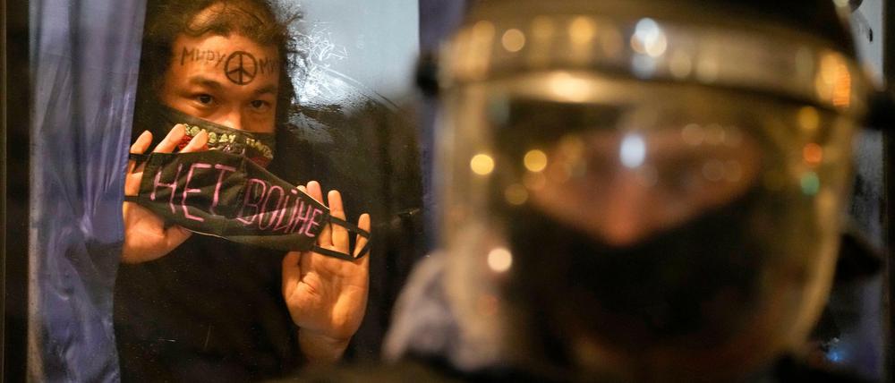 Russland, St. Petersburg: Ein festgenommener Demonstrant zeigt ein Schild mit der Aufschrift «Kein Krieg» aus einem Polizeibus.