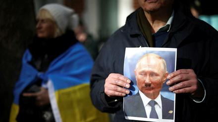 Demonstranten in London haben auf ein Putin-Foto ein Hitler-Bärtchen gemalt.