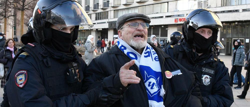 Zwei Uniformierte mit Schutzhelmen führen einen älteren Mann auf einem öffentlichen Platz ab.