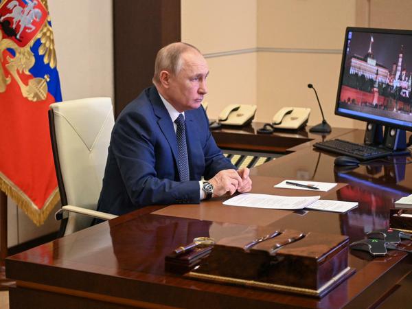 Putin sitzt am Schreibtisch und verfolgt eine Veranstaltung auf einem Bildschirm.