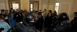 In einem historischen Gebäude steht eine größere Gruppe von Menschen behelmten Uniformierten gegenüber.